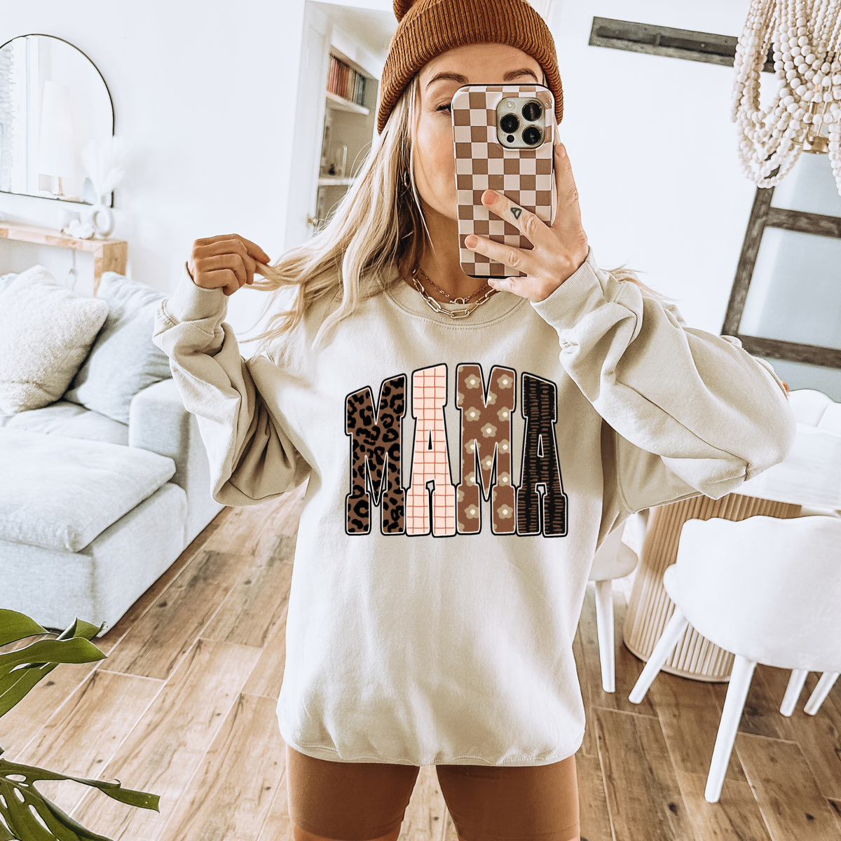 Person wearing a sweatshirt with 'MAMA' in leopard print letters in a cozy living room.