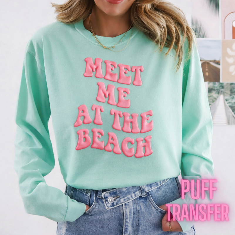 Person wearing a light blue sweatshirt with puff pink text 'MEET ME AT THE BEACH' and denim shorts.